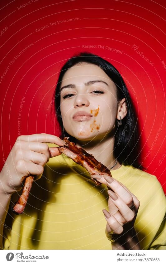 Woman eating ribs with sauce on face against red background woman barbecue messy joyful dining food casual meal meat enjoyment cheerful savory indulgence