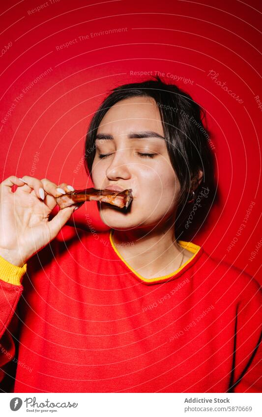 Woman enjoying succulent barbecue ribs against red background woman sweater eating food cuisine enjoyment flavor savory tasty indulgence casual meal dinner