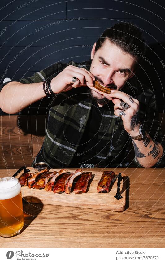 Man enjoying ribs with beer in a casual restaurant setting man tattoo grill barbecue eating style modern food drink meal dining savors grilled table frothy