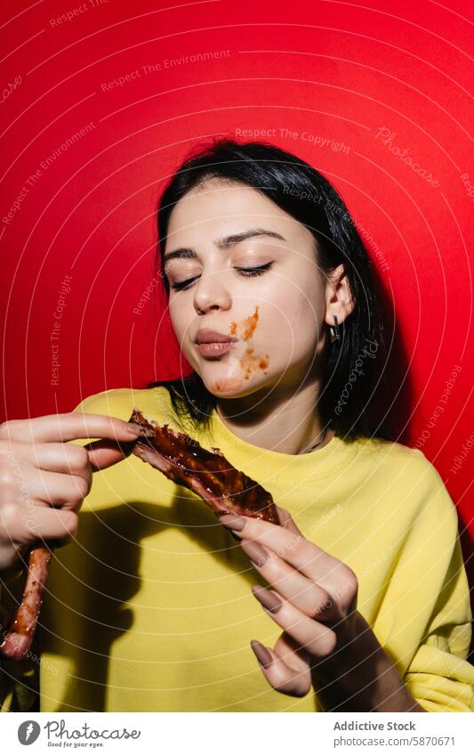 Young woman enjoying delicious ribs against a red background barbecue sauce eating messy enjoyment food meal meat yellow youthful female savory casual