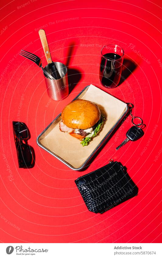 Stylish barbecue-themed meal setup on a vibrant red background burger metal tray knife fork glass beverage stylish savory accessory sunglasses wallet lifestyle