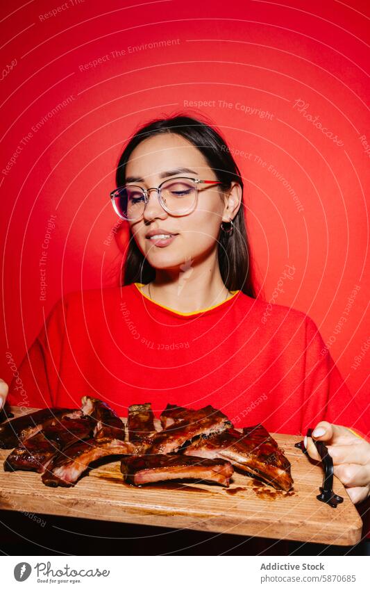 Woman presenting delicious barbecued ribs on a wooden board woman red background food restaurant marketing young vibrant sweater cutting board succulent