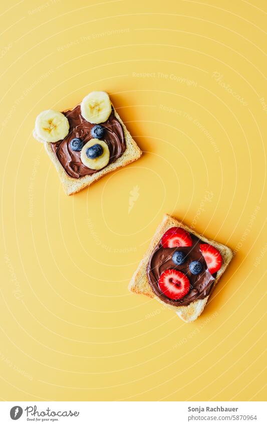 Two slices of toast with chocolate cream and funny animal faces made of fruit. Top view, yellow background. Toast Animal face Funny Breakfast Bread Delicious