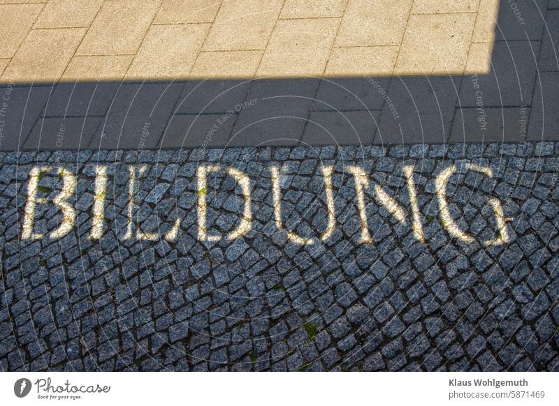 The shadow cast shows the lettering BILDUNG on the granite paving of a path. Or the stony path to education. Education Cobblestones Granite pavers walkway slabs