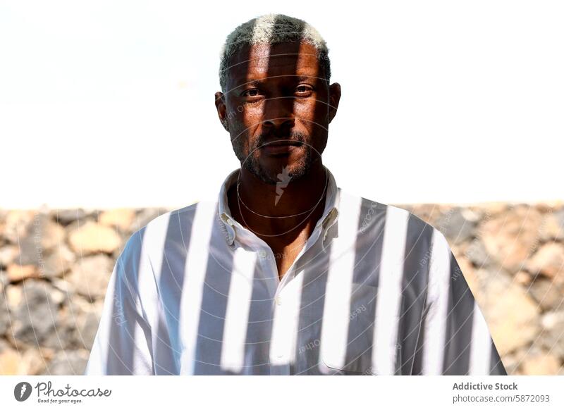 Mature man with graying hair looking directly at camera portrait black outdoor sunlight white shirt serious looking at camera middle-aged calm