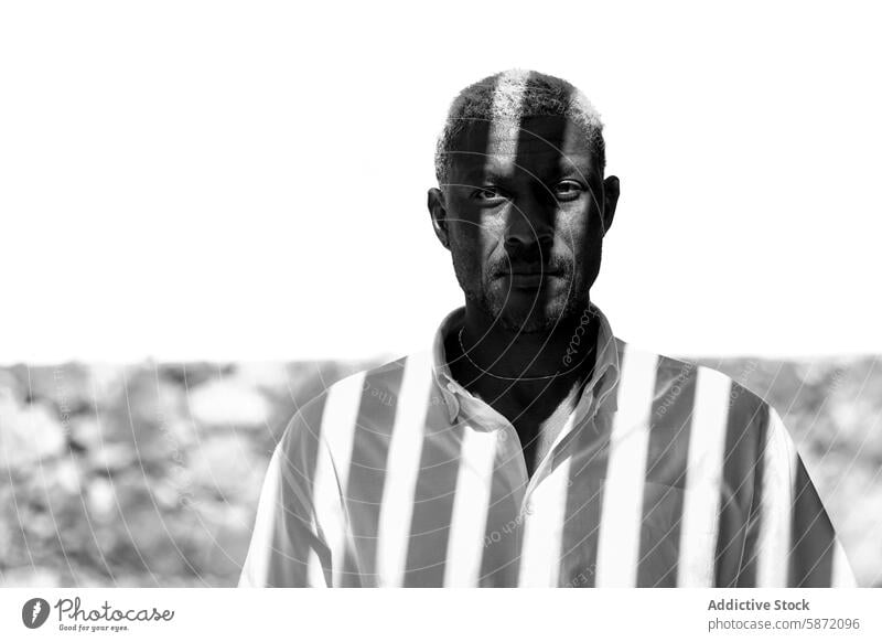 Portrait of a man in a shirt covered by shadow strips in monochrome portrait black and white neutral expression gaze direct close-up african descent male adult