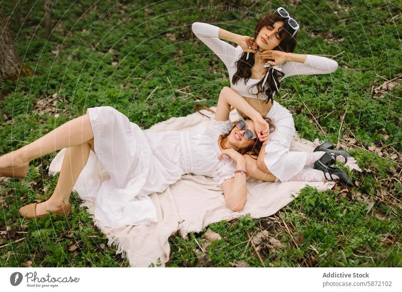 Relaxing moments of two female friends in a forest relaxation nature outdoor woman blanket lying sunglasses happy style white dress leisure peaceful smile grass