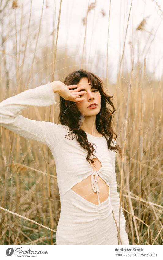 Young woman posing in tall grass in a serene setting young graceful stylish white dress natural woodland artistic mood outdoor hand face dry grass elegance