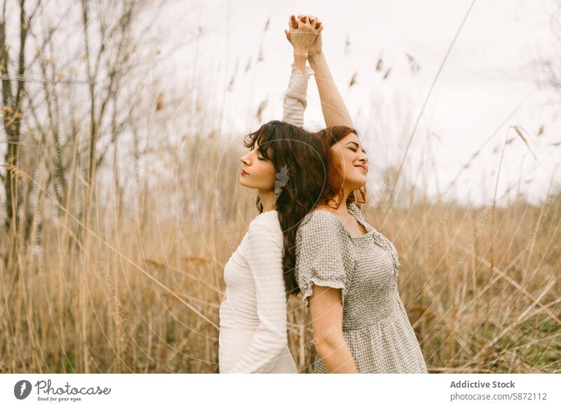 Young women enjoying a serene moment together in the woods woman friend nature tranquil vintage dress back-to-back eyes closed smile natural setting grass