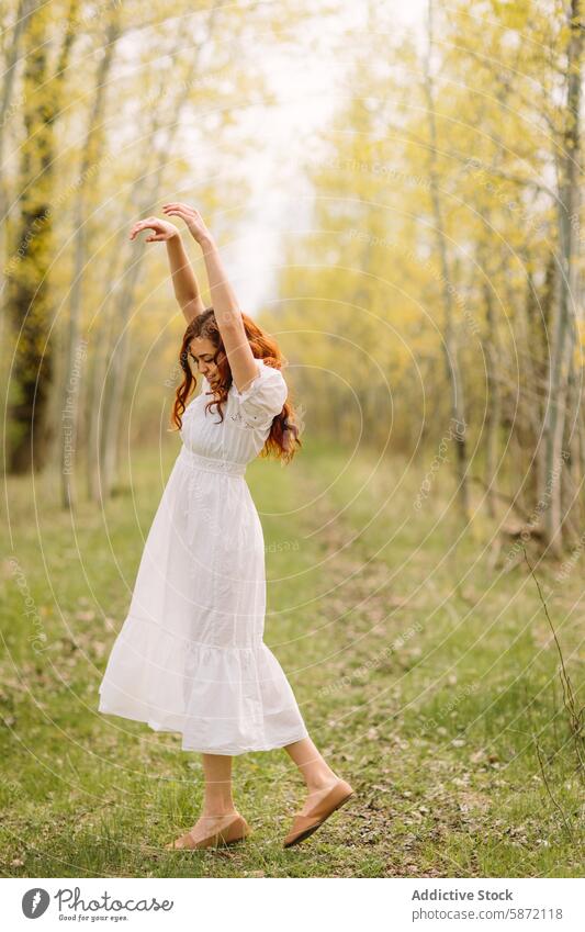 Young woman dancing carefree in a forest setting dance freedom joy nature white dress curly hair red hair happiness outdoor spring youthful greenery tree