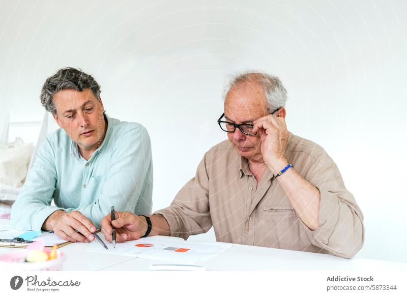 Two men collaborating in a modern coworking space collaboration workspace caucasian male man older adult middle-aged document pen marker table white room focus