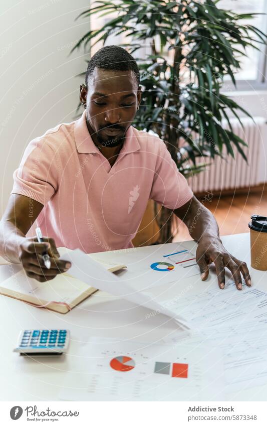 African American man working on project in coworking space african american workspace focused design looking down coffee cup table paper calculation office