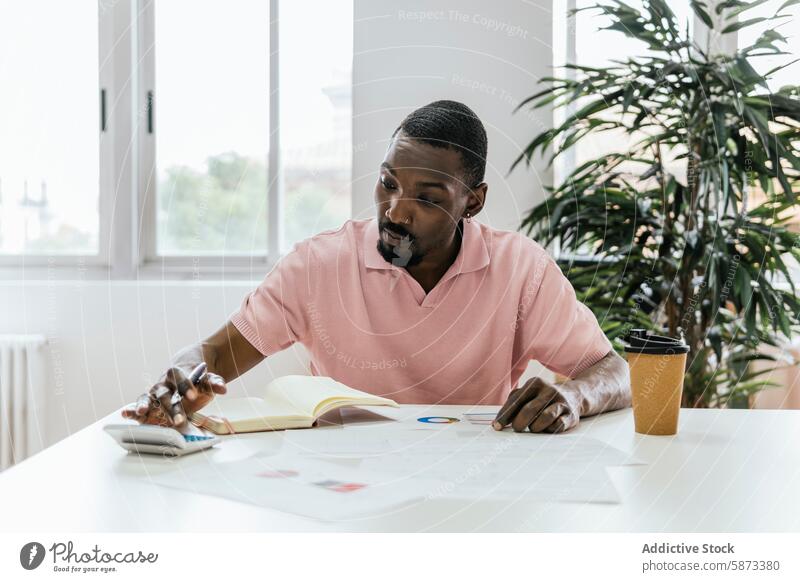 African American man working on project in coworking space african american workspace focused design looking down coffee cup table paper calculation office