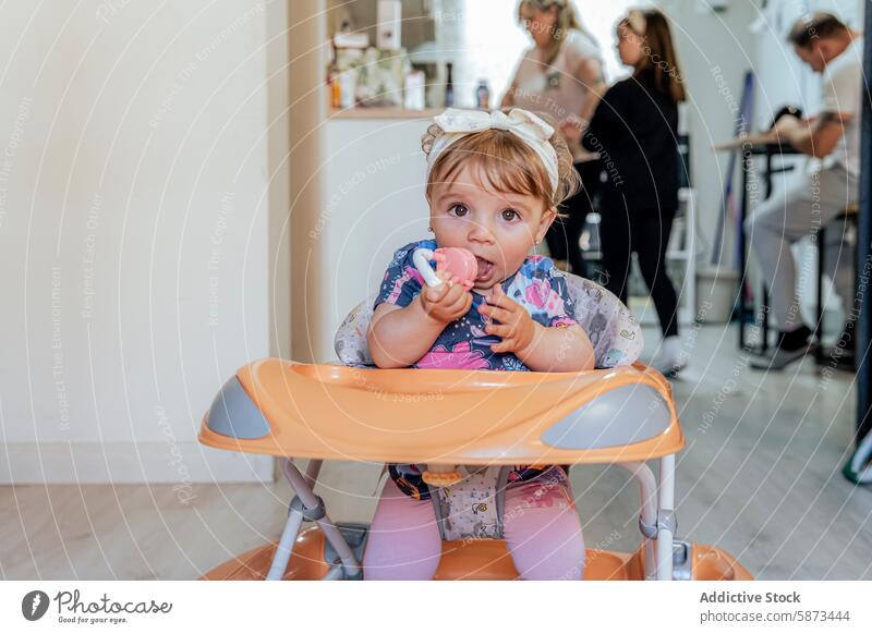 Toddler enjoys a meal in highchair while family is busy in the background toddler kitchen home indoor baby girl toy casual child mealtime domestic lifestyle