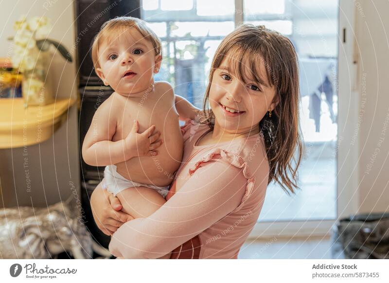 Young girl holding her baby brother at home family indoor sibling smile cozy room child toddler affection care bond love togetherness happy joy cute portrait