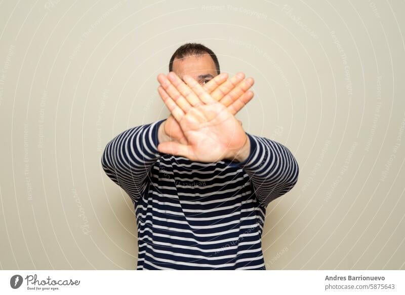 Hispanic man with beard standing over beige background rejection expression crossing arms and palms doing negative sign. symbol denial arrogant casual crucifix