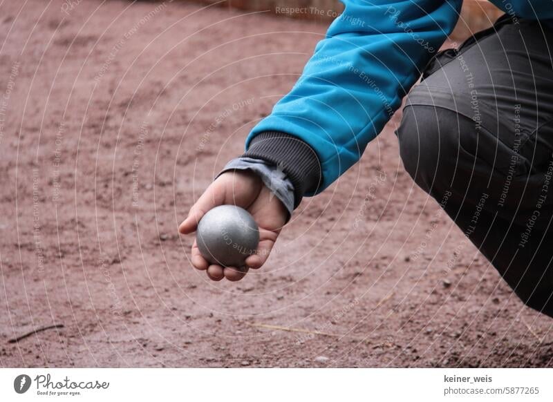 Boules ball in the hand of a boules player playing pétanque or boules on red earth Petanque Sphere Boules player Playing Bouel game Petanque court Boules court