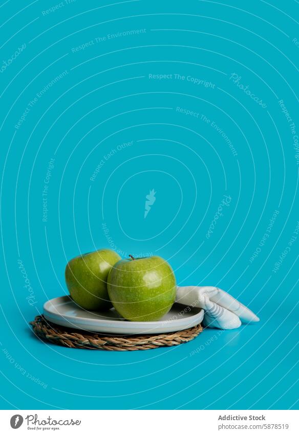 Top view of fresh green apples on blue backdrop plate healthy vibrant simple background fruit mat woven food photography minimalistic composition detail textile