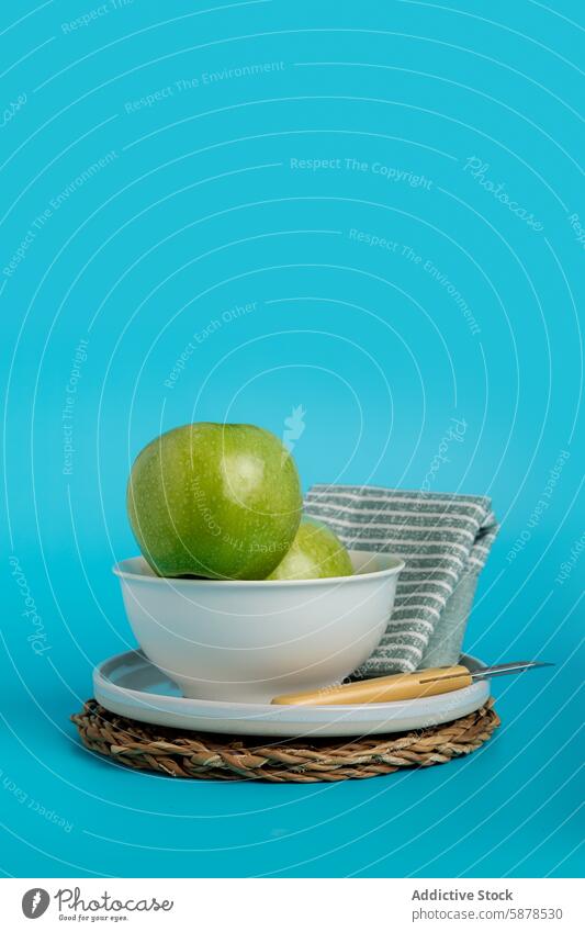 Fresh green apples in white bowl against turquoise backdrop ceramic background straw placemat knife napkin striped fresh crisp fruit snacking healthy natural