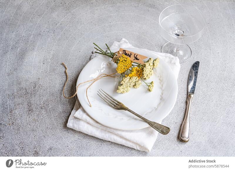 Rustic table setting with achillea and thank you note rustic wildflower white plate fresh vintage silverware glass concrete background summer meadow natural