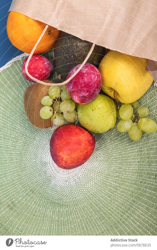 Top view of a colorful assortment of fruits in a paper bag top view fresh orange avocado apple kiwi grape texture green mat vibrant variety healthy nutrition