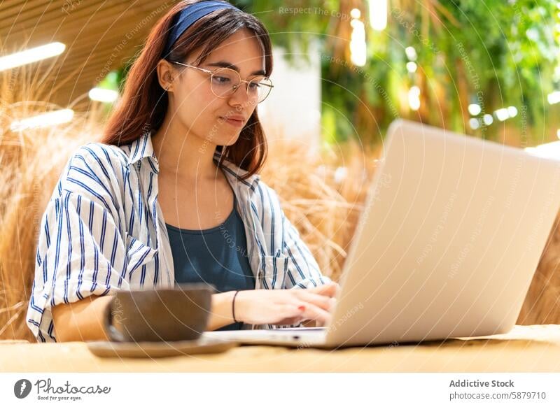 Young woman working on laptop in a natural outdoor setting natural setting productivity technology serene young striped shirt seated focus nature casual glasses