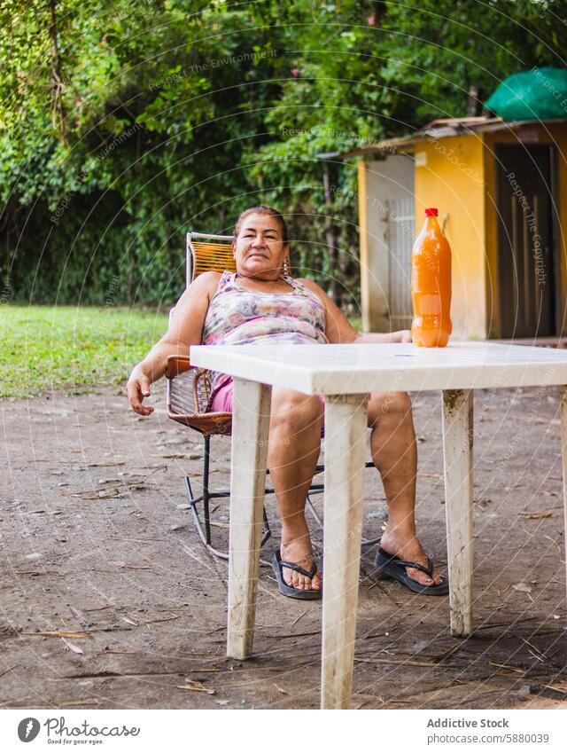 Elderly woman relaxing outdoors with Colombian Guarapo elderly sitting chair colombia bottle drink guarapo sugar cane honey table rural casual nature green