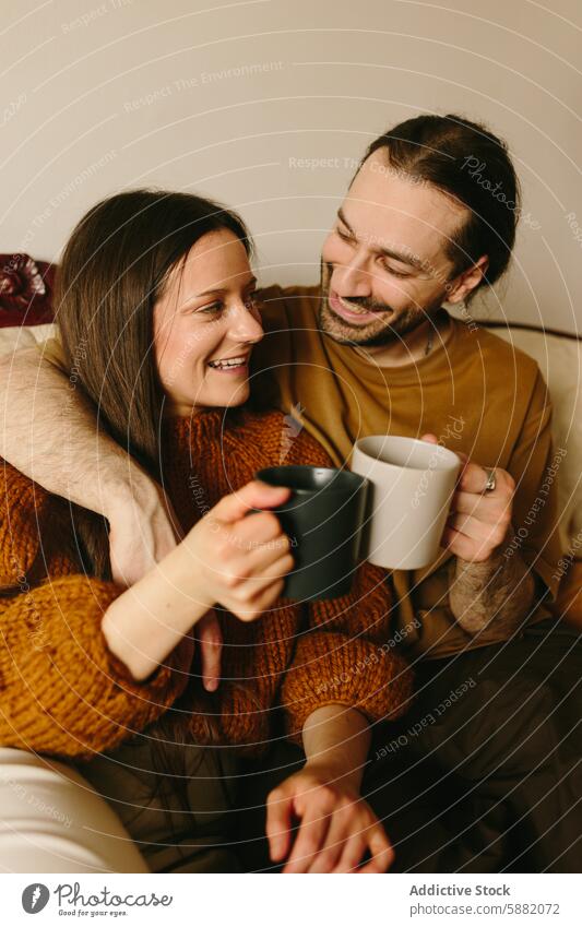 Affectionate couple sharing a cozy moment on a sofa affection love gaze intimate woman caucasian sweater autumn winter hand smile cup coffee tea comfort sitting