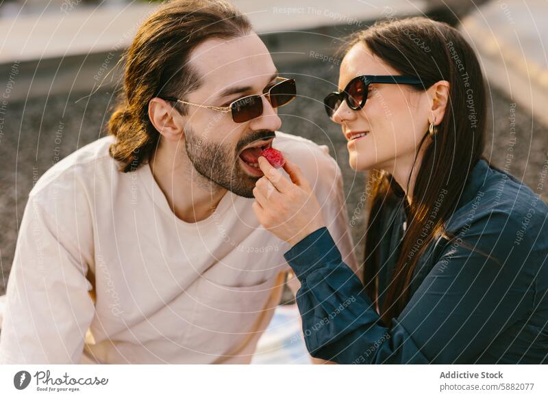 Romantic moment with a couple sharing a strawberry on a rooftop joy sunglasses casual playful woman sunny leisure outdoors feeding food fruit love relationship