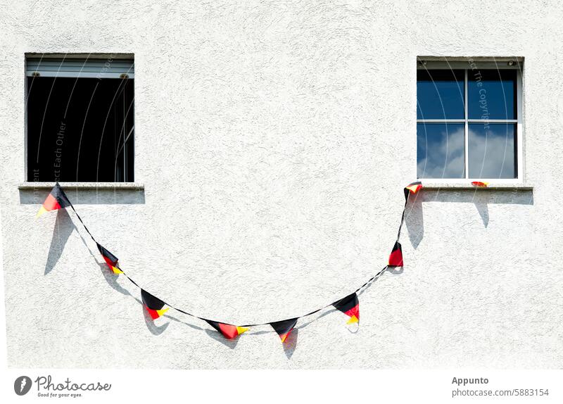 Keep smiling! - For the 2024 European Football Championship, a line of black, red and gold Germany pennants is strung between two windows on a white house façade, giving the impression of a winking smiley face.