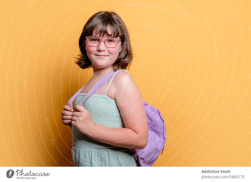 Schoolgirl with glasses and backpack smiling in studio schoolgirl smile yellow background pose child student education happy accessory fashion outfit preschool