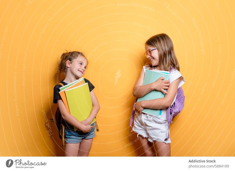 Schoolgirls with books smiling in a studio setting school smile student yellow background backpack eyeglasses education happy cheerful friendship learning