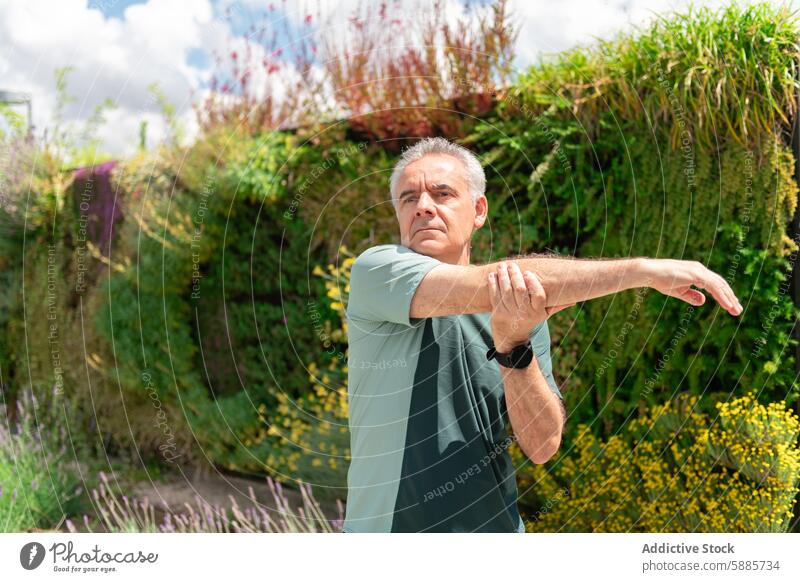 Senior man stretching in a lush green park senior t-shirt exercise fitness wellbeing mature arm preparation vibrant foliage garden health active lifestyle