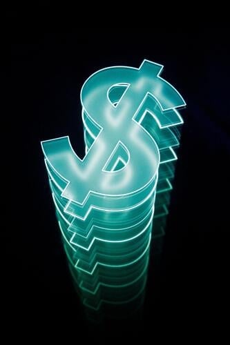 A neon dollar sign with multiple reflections that stands out brightly from the darkness. Money Capitalism capital finance financial world currency Americas