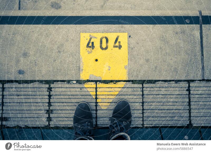 A bright yellow marker with the inscription "404" on the concrete slabs of a pedestrian path. The surroundings are blue and you can see the photographer's winter shoes.