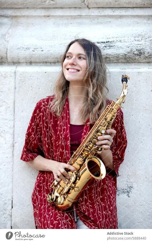 Woman happily playing saxophone in stylish outfit woman music joyful caucasian red jumpsuit smile style musician urban background performance instrument happy