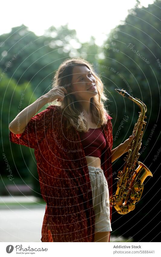 Young woman holding saxophone in sunny park setting music musician sunlight summer young caucasian female outdoor leisure hobby instrument brass saxophonist