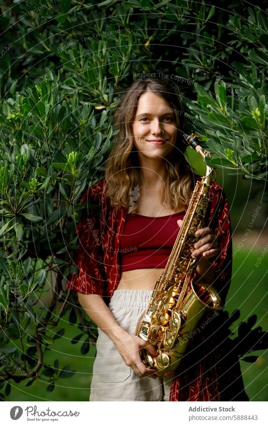 Woman holding saxophone in a lush garden woman music musician green foliage smile cheerful friendly looking at camera saxowoman instrument brass jazz