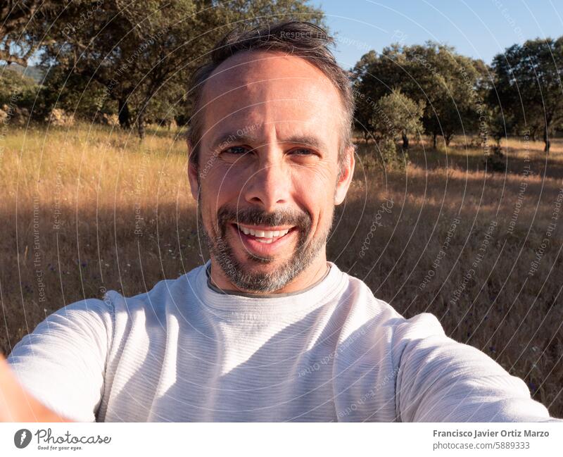 Man Taking Selfie in Sunny Countryside Landscape smile happy selfie man countryside nature landscape field outdoor sunny trees sky portrait photography travel