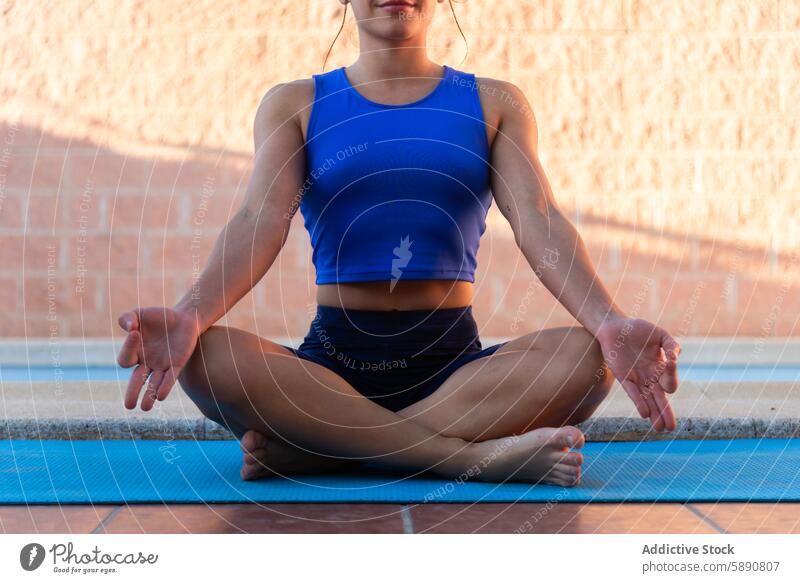 Young woman practicing meditation near a swimming pool yoga mindfulness tranquility blue mat sportswear fitness health wellness outdoor serene calm focused