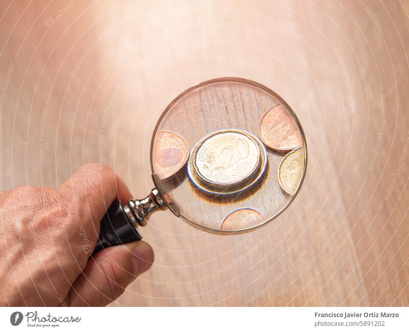 Hand Holding Magnifying Glass Over Coins magnifying glass coin hand closeup detail examination inspection scrutiny numismatics currency money finance collection
