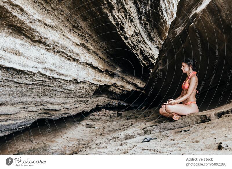 Woman meditating in serene rocky cave on summer holiday woman meditation tranquility retreat bikini red young peaceful secluded nature relaxation mindful