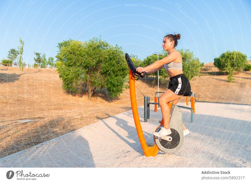 Young woman training on outdoor fitness equipment exercise gym street bike health sport active lifestyle wellness young female athletic workout physical