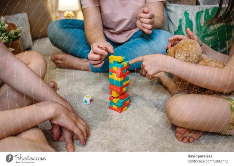 Unrecognizable family having fun playing with wooden stacking piece game over carpet at home unrecognizable together children tower little girl pointing finger