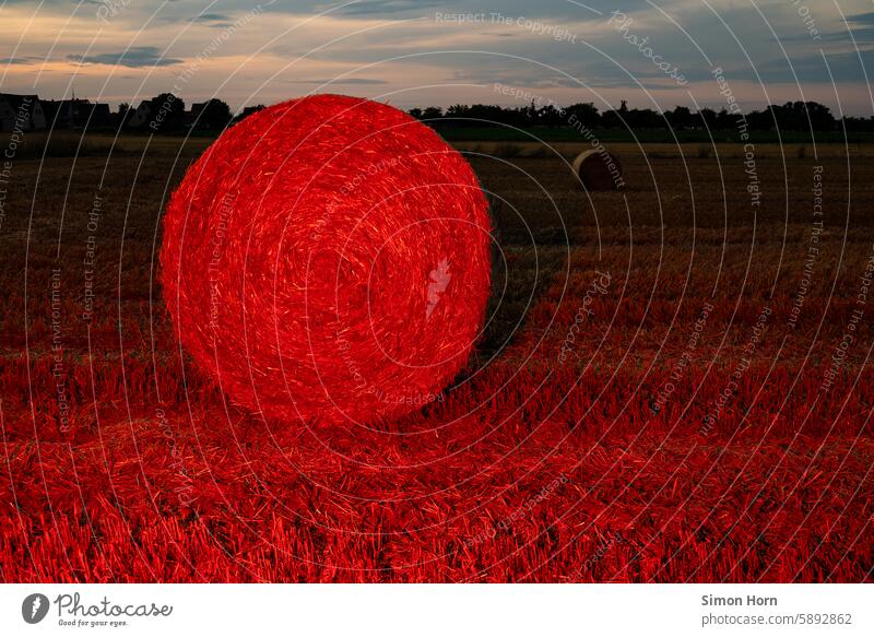 Straw bales in red lighting against a calm evening sky and village silhouette Bale of straw Red light Harvest Agriculture Village Romanticism rural