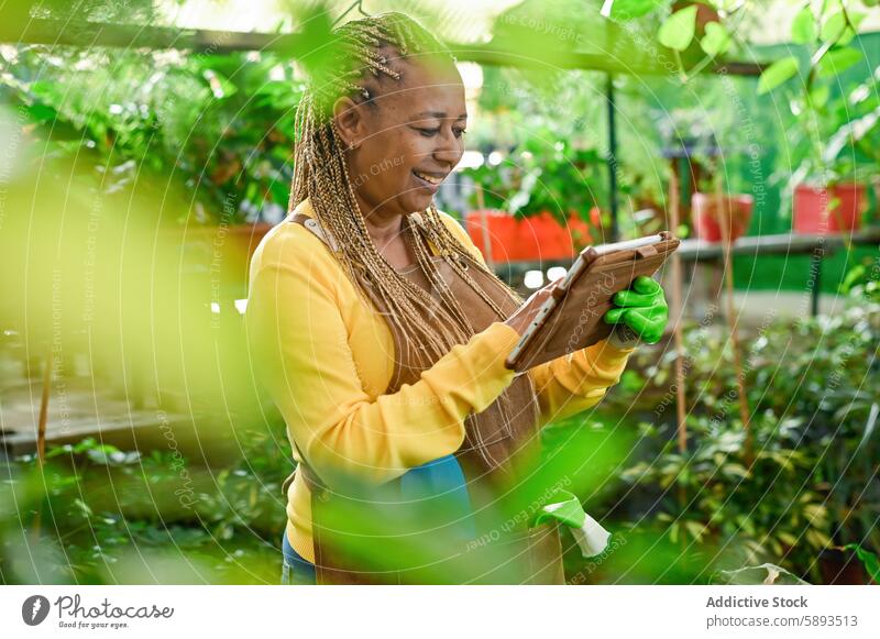 Cheerful ethnic woman using tablet greenhouse smile happy cheerful gadget device internet female modern browsing plant joy positive glad hothouse garden