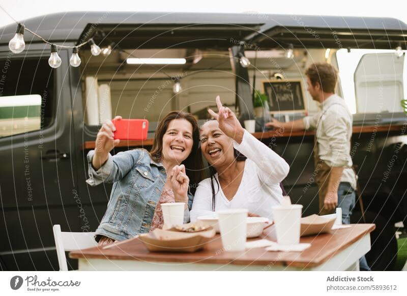 Adult women taking selfie near food truck happy lunch smartphone together two fingers smile v sign female optimist glad self portrait positive cheerful memory