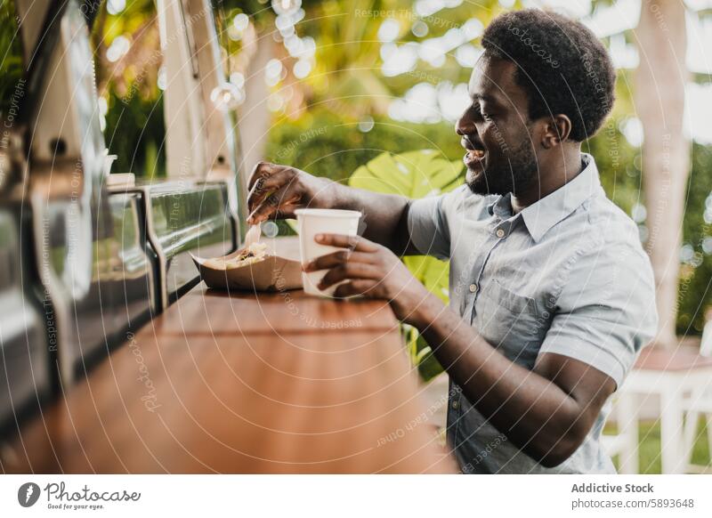 Young african man eating in food truck counter outdoor in city park - Focus on face african american bar beverage black cultural customer delivery dinner drink