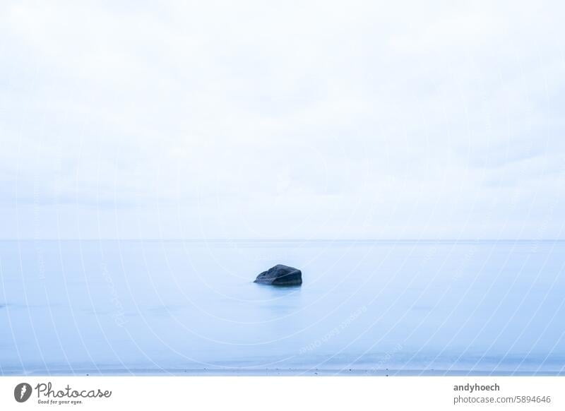 A solitary rock in the sea in a soft blue colour beach beauty blur boulder calm cloudy coast coastline dramatic dream emptiness empty endless environment