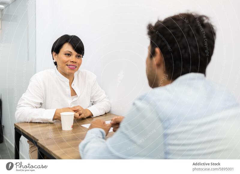 Interactive meeting between two colleagues at a table woman conversation office professional collaborative academic discussion white shirt coffee cup bright